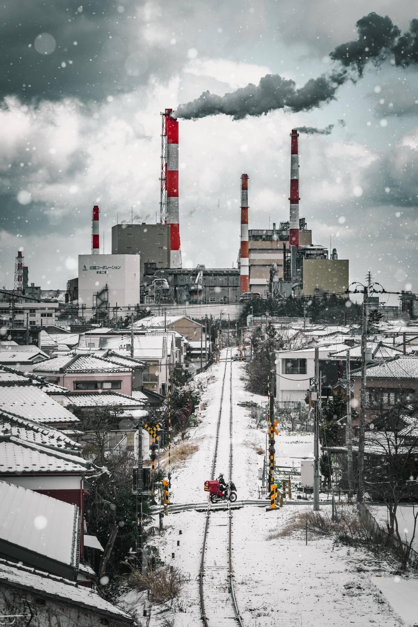 雪の線路の先に、紅白の煙突と住宅が並ぶ