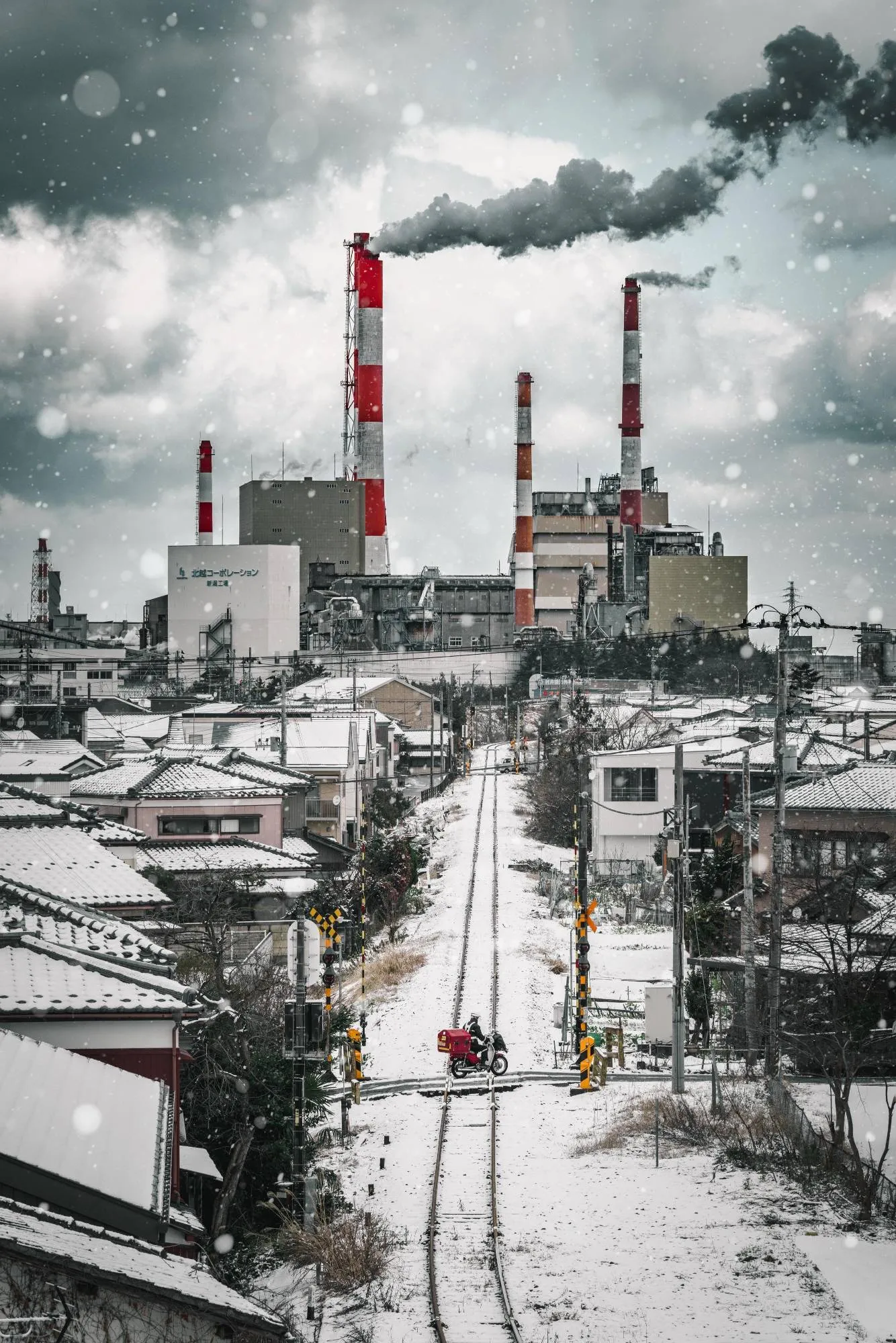 雪の線路の先に、紅白の煙突と住宅が並ぶ